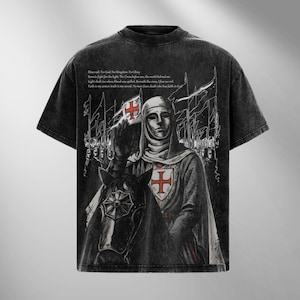 May include: Black graphic t-shirt featuring a medieval knight on horseback holding a flag with a red cross. The design includes text and a distressed, vintage aesthetic. The shirt has a crew neck and short sleeves.