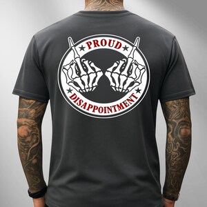 May include: Dark grey t-shirt with a white circular graphic on the back. The graphic features two skeleton hands giving the middle finger, with the words "PROUD" and "DISAPPOINTMENT" in red.