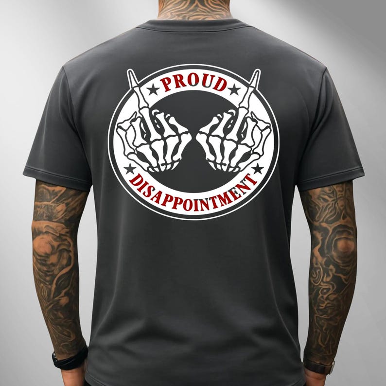May include: Dark grey t-shirt with a white circular graphic on the back. The graphic features two skeleton hands giving the middle finger, with the words "PROUD" and "DISAPPOINTMENT" in red.