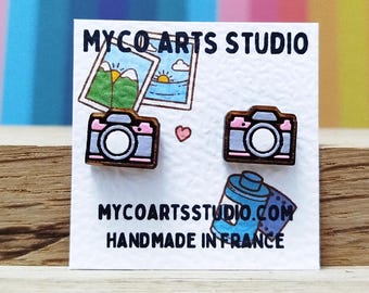 Op de afbeelding: Houten oorbellen in de vorm van een camera, met roze en grijze accenten, gepresenteerd op een witte kaart. De kaart toont de tekst "MYCO ARTS STUDIO" en "HANDMADE IN FRANCE". Een klein roze hartje is ook zichtbaar.