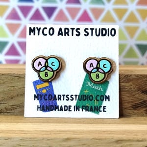 Op de afbeelding: Houten oorstekers met een Venn-diagramontwerp, met de letters A, B en C in roze, blauw en groen. De oorbellen staan op een witte kaart met de tekst "MYCO ARTS STUDIO" en "MYCOARTSSTUDIO.COM HANDMADE IN FRANCE".