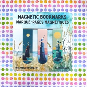 Op de afbeelding: Een set van drie rechthoekige magnetische bladwijzers op een kaart met de tekst MAGNETIC BOOKMARKS MARQUE-PAGES MAGNÉTIQUES. Elke bladwijzer toont een kusttafereel met een meeuw op een rotsformatie tegen een zonnige lucht.