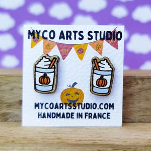 Op de afbeelding: Een paar houten oorbellen in de vorm van pumpkin spice lattes met slagroom en een kaneelstokje. De oorbellen zijn op een witte kaart met de tekst "MYCO ARTS STUDIO.COM HANDMADE IN FRANCE".