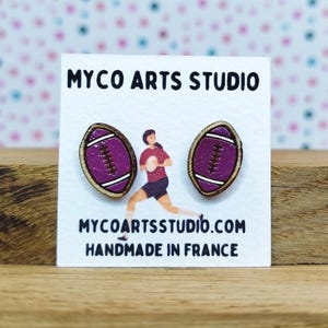 Op de afbeelding: Een paar paarse en bruine rugbybalvormige oorknopjes. De oorbellen staan op een witte kaart met de tekst "MYCO ARTS STUDIO" en "MYCOARTSSTUDIO.COM HANDMADE IN FRANCE".
