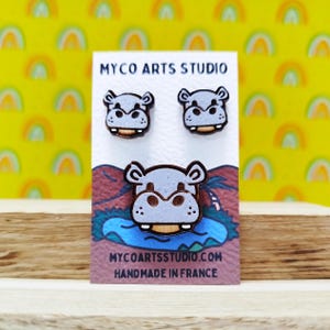 Könnte beinhalten: Ein Paar Holzohrringe mit einem Cartoon-Nilpferd-Design. Die Ohrringe sind handgefertigt in Frankreich und werden von Myco Arts Studio verkauft.