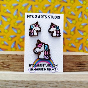 Op de afbeelding: Een paar houten unicorn oorbellen met roze, blauwe en witte details. De oorbellen zijn handgemaakt in Frankrijk en worden verkocht door Myco Arts Studio.