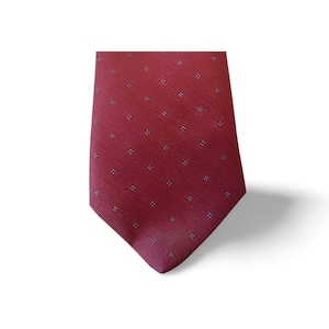 Puede incluir: Una corbata burdeos con un patrón repetido de pequeños puntos blancos y negros. La corbata está hecha de una tela suave y se muestra sobre un fondo blanco. Un accesorio clásico para vestimenta formal o de negocios.