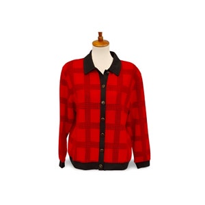 May include: A red plaid cardigan with a black collar, cuffs, and button placket. The long-sleeved sweater is displayed on a mannequin. The plaid pattern is a dark red and black. The cardigan has six black buttons.
