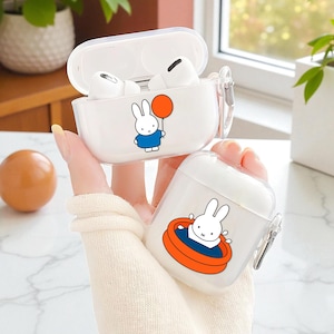 Op de afbeelding: Twee doorzichtige witte AirPod-hoesjes met cartoonkonijn-afbeeldingen. Eén hoesje is open en onthult witte oortelefoons. Het andere hoesje heeft een konijn in een zwembad. Beide hoesjes hebben een transparant plastic ontwerp en een zilveren sluiting.