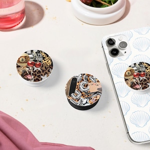 May include: Two phone grips with a leopard print and colorful accents. One grip features a cherry and a playing card, the other features a skateboard and a silver chain.