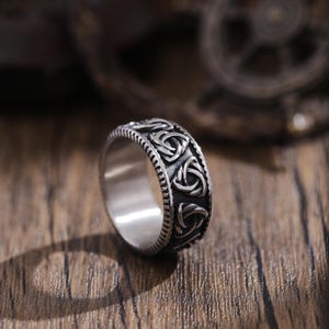 Könnte beinhalten: Ein silberner Ring mit einem keltischen Knotendesign. Der Ring liegt auf einer Holzoberfläche.