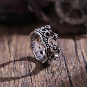 Könnte beinhalten: Ein silberner Kronenring mit filigranen Details. Der Ring ist aus Metall und hat eine polierte Oberfläche.