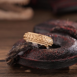 Peut inclure: Une bague en or avec un motif texturé. La bague est en métal lisse et brillant et présente un motif détaillé d'écailles qui se chevauchent.