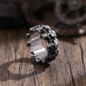 May include: A silver ring with a design of multiple skulls around the band.