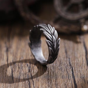 May include: A silver ring with a leaf design. The ring is made of metal and has a textured finish.