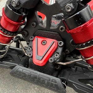 May include: Close-up of a black and red remote control car chassis. Features include red coil-over shocks, silver springs, and a black chassis with a red accent piece. The car has a number 68 on the side.