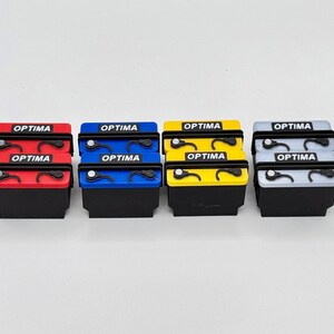 May include: Four Optima battery replicas in red, blue, yellow, and gray. Each battery has the word "OPTIMA" printed on the top and bottom. The batteries are black on the bottom and have a detailed top.