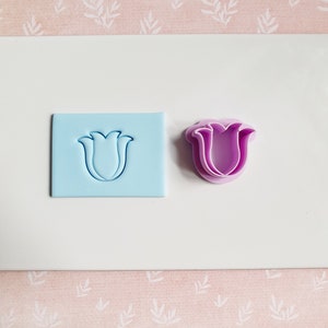 May include: A set of two cookie cutters, one blue and one purple, shaped like a tulip.