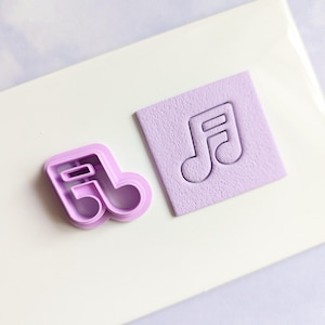 Könnte beinhalten: Ein violetter Plastik-Ausstecher in Form einer Musiknote, neben einem violetten Abdruck der Note in einem Quadrat aus violettem Fondant.