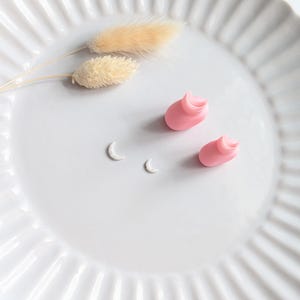May include: A white, fluted plate holds two pink, curled objects, two small white crescent shapes, and two dried, beige flower stems. The arrangement is simple and elegant, with a focus on delicate details and soft colors.