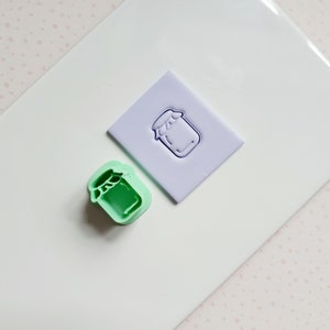 May include: A green plastic cookie cutter shaped like a jar with a lid. A purple rubber stamp with the same jar design is also shown.