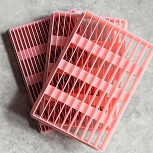 Può includere: Quattro vassoi di plastica rosa con un motivo a griglia. I vassoi sono impilati uno sopra l'altro.