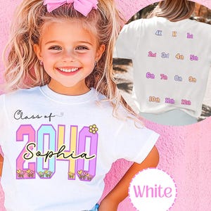 May include: A white t-shirt featuring the text Class of 2040 with the name Sophia in cursive script. The numbers are filled with pastel colors and small flower graphics. The back of the shirt displays a list of school grades from 4K to 12th.