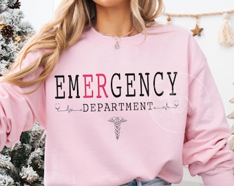 May include: Light pink sweatshirt with the words "EMERGENCY DEPARTMENT" in black and red lettering. A medical caduceus symbol is below the text. The sweatshirt is a light pink color.