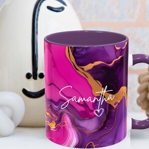 Pode incluir: Caneca de caf&eacute; roxa e rosa com um design de redemoinho dourado e o nome Samantha escrito em branco. A caneca tem um interior roxo.