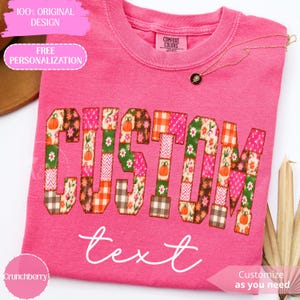 Puede incluir: Una camiseta de manga corta de color rosa brillante con la palabra CUSTOM en letras grandes de bloque rellenas con un patrón de patchwork de calabazas, flores y cuadros. Debajo, la palabra text está escrita en cursiva blanca.
