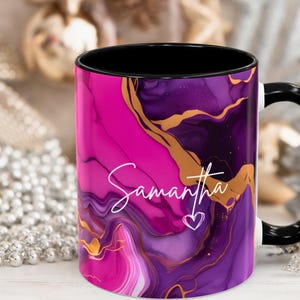 Pode incluir: Uma caneca de cer&acirc;mica rosa e roxa com al&ccedil;a preta e um design de redemoinho dourado. A caneca tem o nome "Samantha" escrito nela em it&aacute;lico branco.