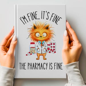 Könnte beinhalten: Ein weißes Notizbuch mit einer gezeichneten orangefarbenen Katze, die einen weißen Laborkittel trägt und eine Pilleflasche hält. Der Text auf dem Notizbuch lautet "Mir geht es gut, alles ist gut, die Apotheke ist gut."