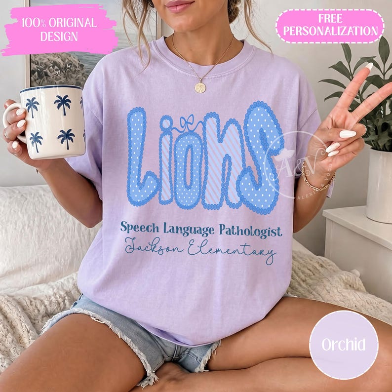 K&ouml;nnte beinhalten: Ein hellviolettes T-Shirt mit dem Wort Lions in gro&szlig;en blauen gepunkteten Buchstaben mit einer kleinen Schleife, gefolgt von dem Text Speech Language Pathologist und Jackson Elementary in blauer Schrift, dazu eine wei&szlig;e Tasse mit blauen Palmen.