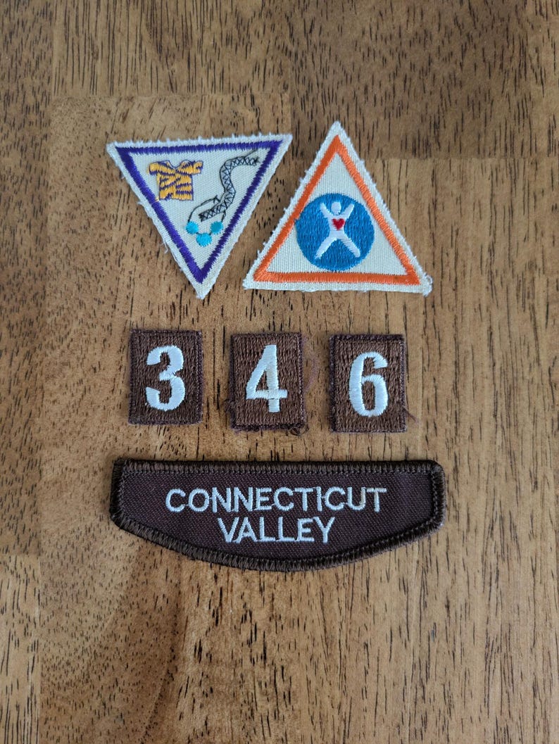 May include: A collection of embroidered patches and badges, including two triangular patches with colorful designs and three rectangular patches with the numbers 3, 4, and 6. A brown patch with the text "CONNECTICUT VALLEY" is also present.