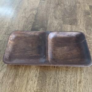 May include: A wooden serving tray with two separate compartments. The tray is dark brown and has a smooth, polished finish.