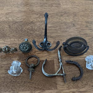 May include: Assortment of vintage hardware including a black metal hook, a crystal knob, a brass knob, a brass pull, and a brass door handle.