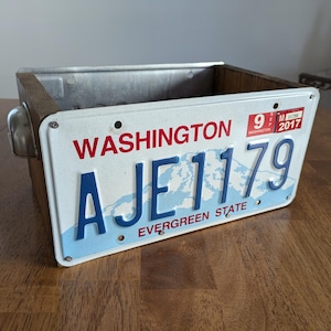 May include: A wooden box with a metal top and a Washington state license plate attached to the front. The license plate is white with blue lettering and reads "AJE 1179" with the words "Washington" and "Evergreen State" printed on the plate.