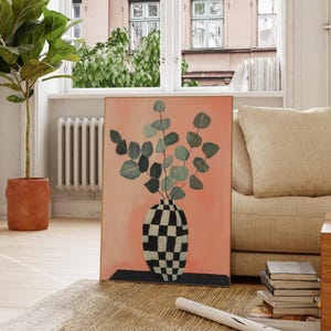 Puede incluir: Una pintura de un jarrón con un patrón de cuadros blanco y negro lleno de hojas verdes sobre un fondo melocotón.