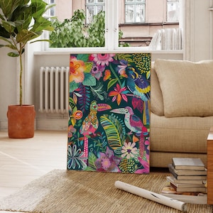 Könnte beinhalten: Ein farbenfroher Leinwanddruck mit tropischem Design. Er zeigt Tukane, Blumen und Blätter in Rosa, Blau, Grün und Gelb vor einem dunklen Hintergrund. Das Kunstwerk wird in einem hellen Wohnzimmer ausgestellt.