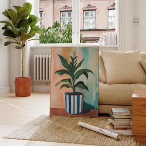 Op de afbeelding: Een woonkamer interieur met een beige bank, een houten salontafel en een groot schilderij van een plant in een blauw-wit gestreepte pot. Het schilderij hangt aan een witte muur.