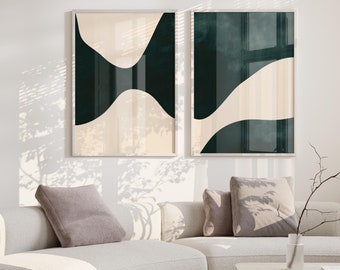 May include: Two abstract art prints with black and white shapes on a cream background. The prints are framed in a thin, silver frame and are hanging on a white wall above a light gray curved sofa with pillows.