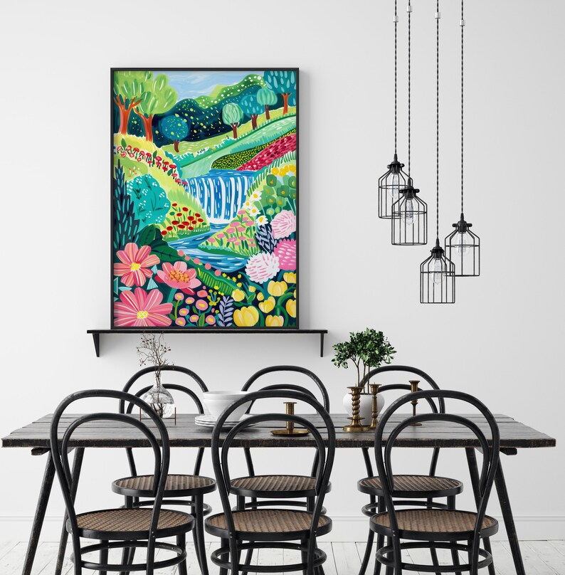 May include: A colorful painting of a waterfall in a lush green forest with pink, yellow, and blue flowers. The painting is framed in black and hanging on a white wall above a wooden table with black chairs.