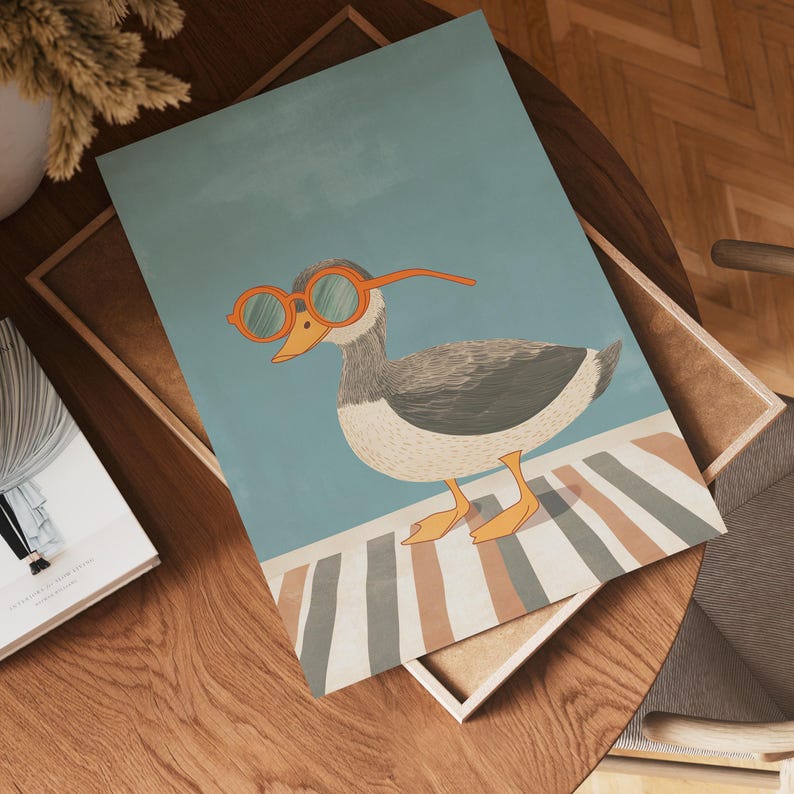 May include: A whimsical illustration of a goose wearing orange sunglasses. The goose is depicted with gray, white, and orange tones, standing on a striped surface against a light blue background. The artwork is presented in a wooden frame.