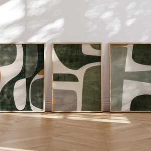 Op de afbeelding: Drie ingelijste abstracte kunstprints met een groen, wit en oranje kleurenschema. De prints tonen organische vormen en texturen.