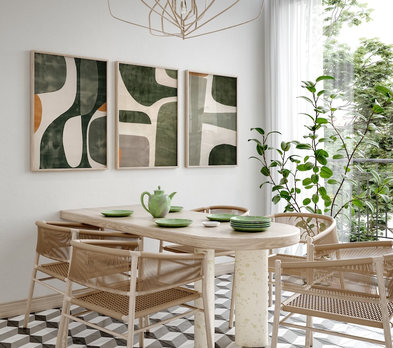 Op de afbeelding: Een eetkamer met een houten tafel en stoelen, een groene theepot en drie abstracte kunstprints met groene en witte geometrische vormen.