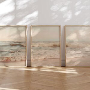 May include: Three framed prints of a beach scene with waves crashing on the shore. The prints are in a light brown frame and have a soft, muted color palette.