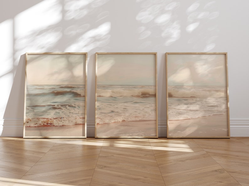 May include: Three framed prints of a beach scene with waves crashing on the shore. The prints are in a light brown frame and have a soft, muted color palette.