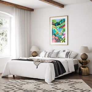 May include: A white bed with a black throw blanket and patterned pillows in a bedroom with a large painting of a colorful landscape with a waterfall and flowers above the bed. Two lamps with gold bases are on nightstands on either side of the bed.