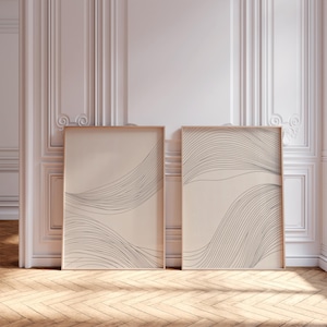 Könnte beinhalten: Zwei gerahmte abstrakte Linienkunstdrucke mit beigefarbenem Hintergrund und schwarzen Linien. Die Drucke sind in Holzrahmen gefasst und hängen an einer weißen Wand.