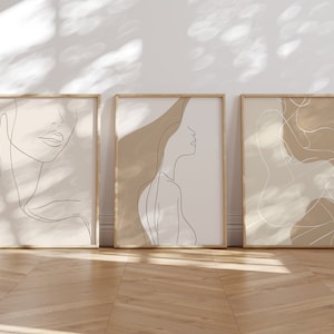 May include: Three framed minimalist line art prints with a beige background. The prints feature abstract line drawings of a face, a figure, and a body.